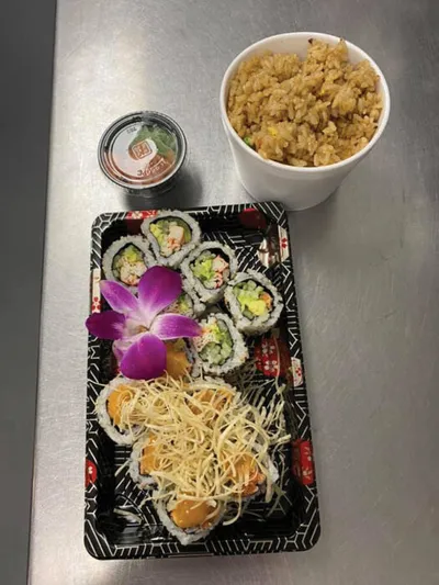 Sushi rolls and fried items on a black tray with a purple orchid, beside a cup of fried rice
