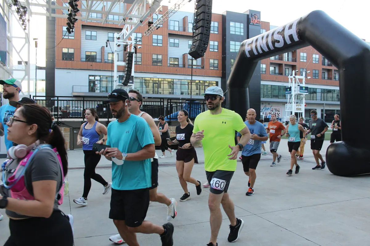Runners crossing a black inflatable finish line arch at an outdoor road race