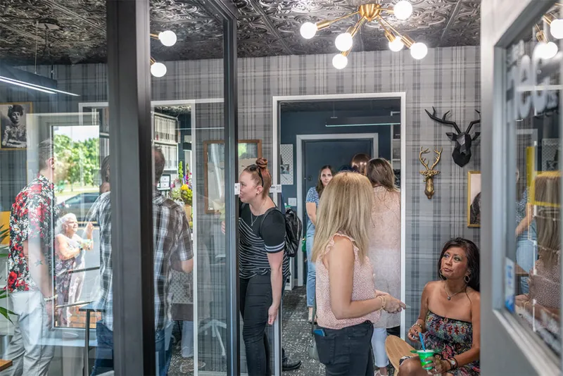 Guests mingling inside a boutique interior design studio with plaid wallpaper and a brass sputnik chandelier