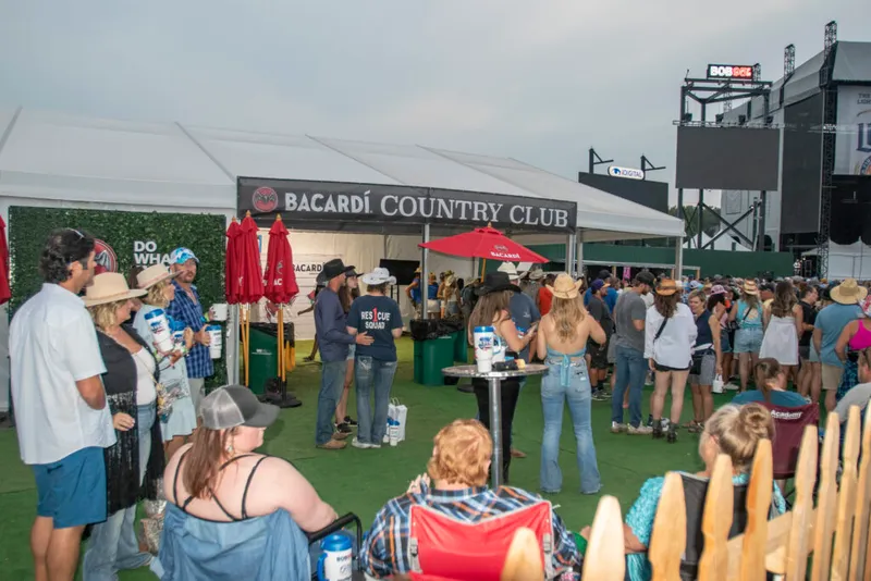 Crowd of festivalgoers gathered at an outdoor Bacardí Country Club tent at a music festival