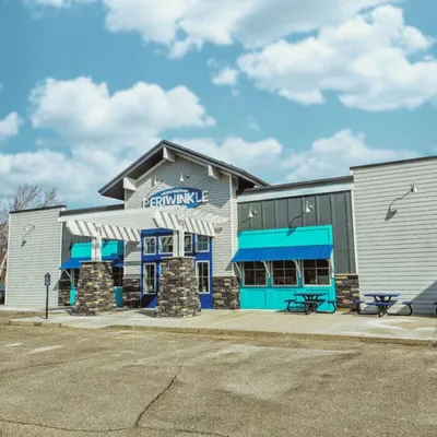 Periwinkle restaurant exterior with teal awnings and stone accents under a partly cloudy sky