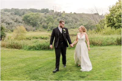 Bride and groom holding hands walking across a green lawn with rolling hills behind them