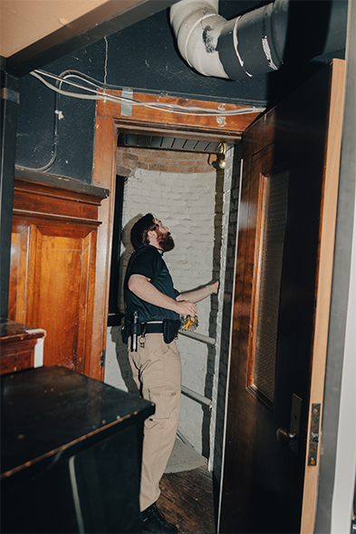 Bearded man in black shirt looks up through a doorway in a dimly lit historic building under renovation