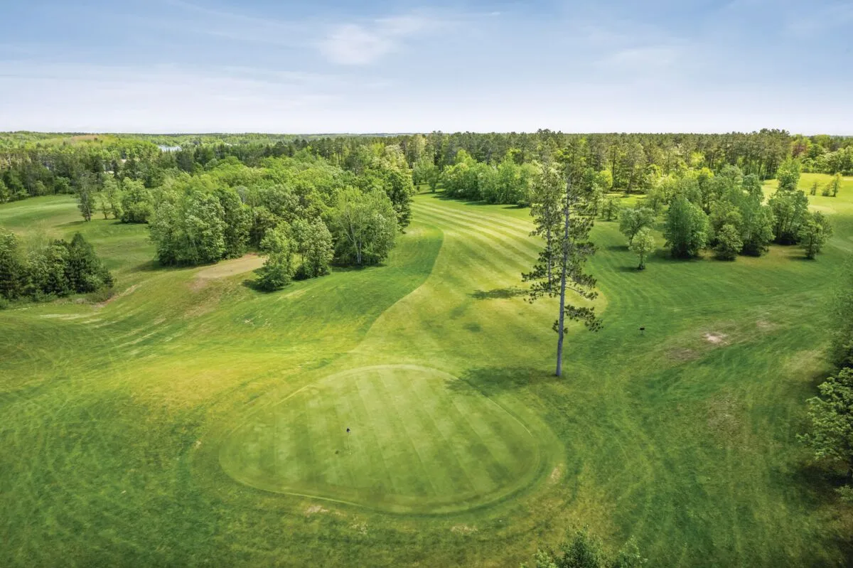 Aerial view of a golf course green surrounded by rolling fairways and dense trees