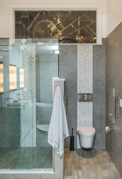 Modern bathroom with glass shower, wall-mounted toilet, gray tile, and decorative patterned accent tile