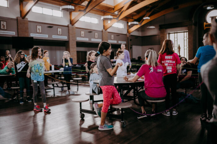 Girls and mentors participate in a group activity inside a large indoor hall