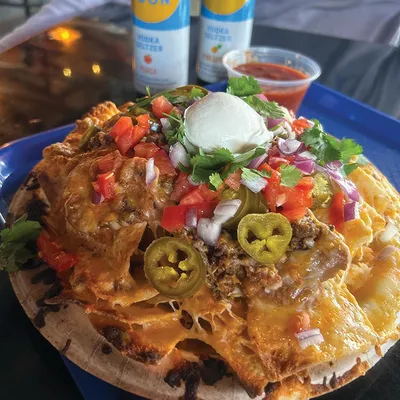 Loaded nachos topped with melted cheese, jalapeños, pico de gallo, sour cream, and cilantro on a blue plate