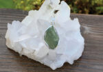 Green gemstone pendant resting against a white crystal cluster