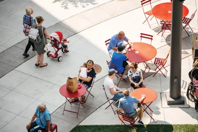 Overhead view of people gathered at red outdoor café tables on a sunny plaza