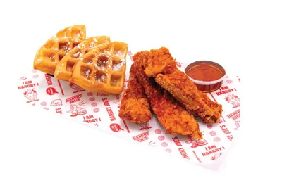 Crispy chicken tenders with waffles and a dipping sauce on branded deli paper