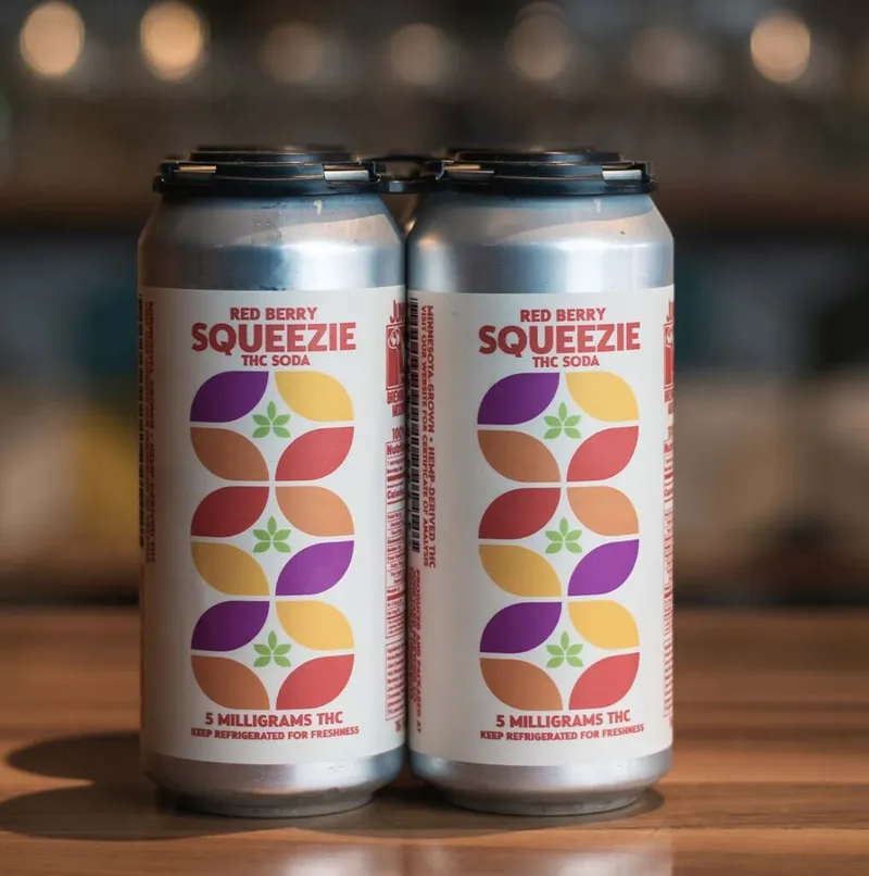 Four-pack of Red Berry Squeezie THC soda cans with colorful petal graphic labels on a wooden surface