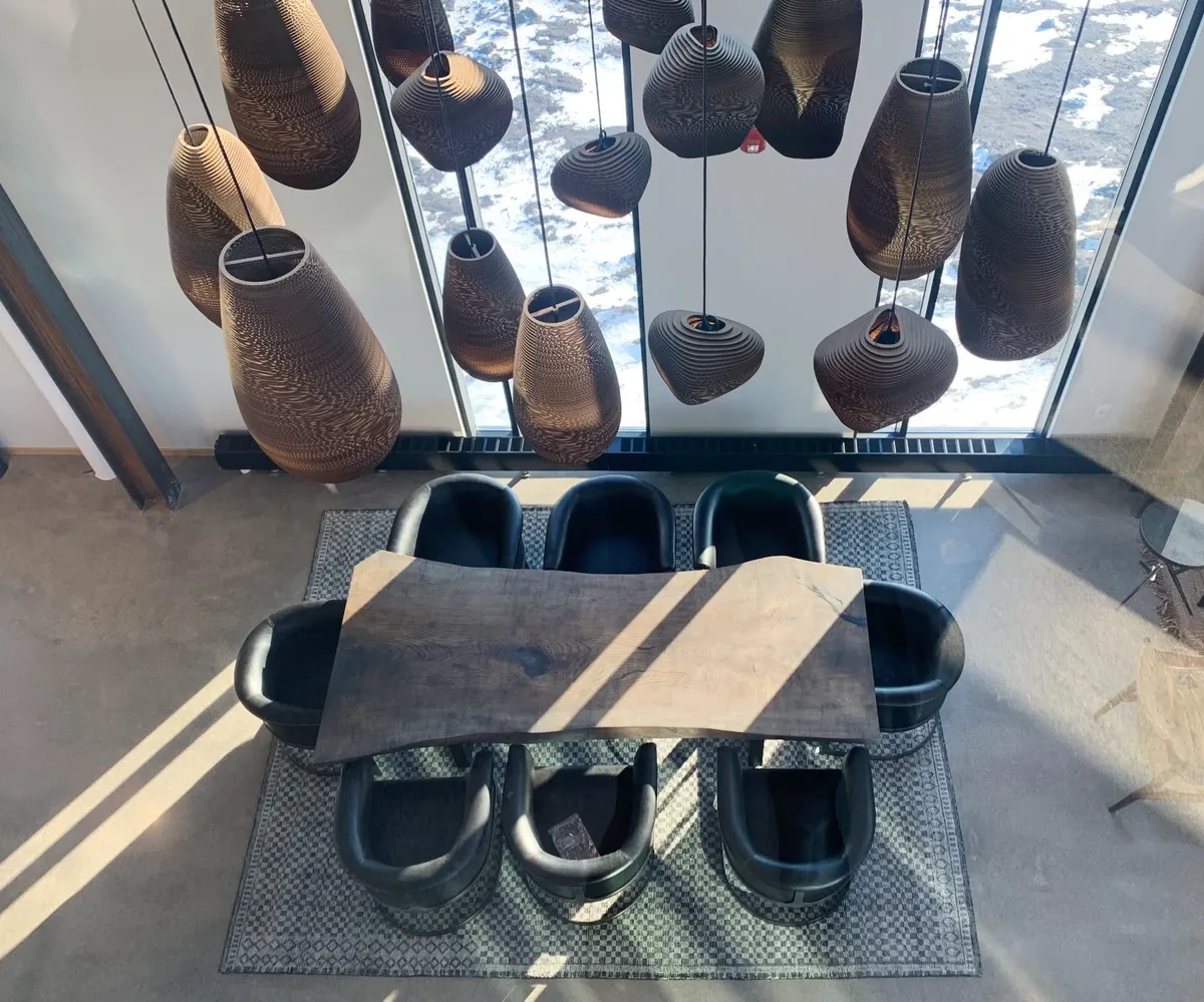 Overhead view of a live-edge wood dining table with black sculpted chairs beneath hanging woven pendant lights