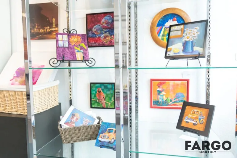 Glass display shelves holding colorful small paintings including a parrot, vintage car, and floral still life