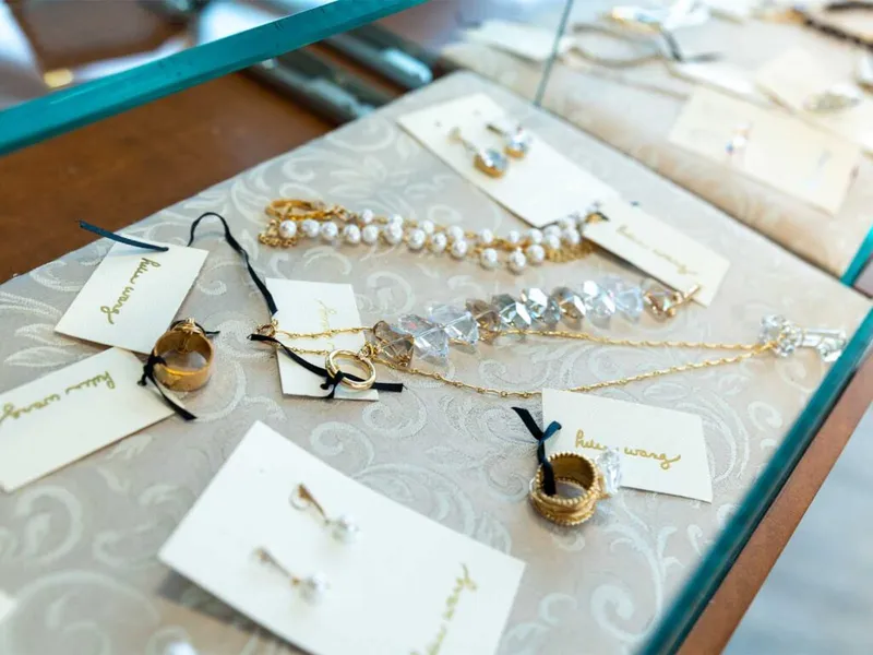 Gold rings, pearl bracelet, crystal jewelry, and earrings displayed on a glass boutique case