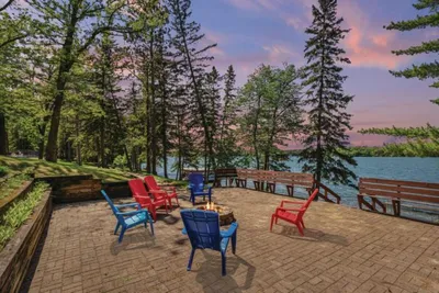 Colorful Adirondack chairs around a fire pit on a lakeside patio at dusk