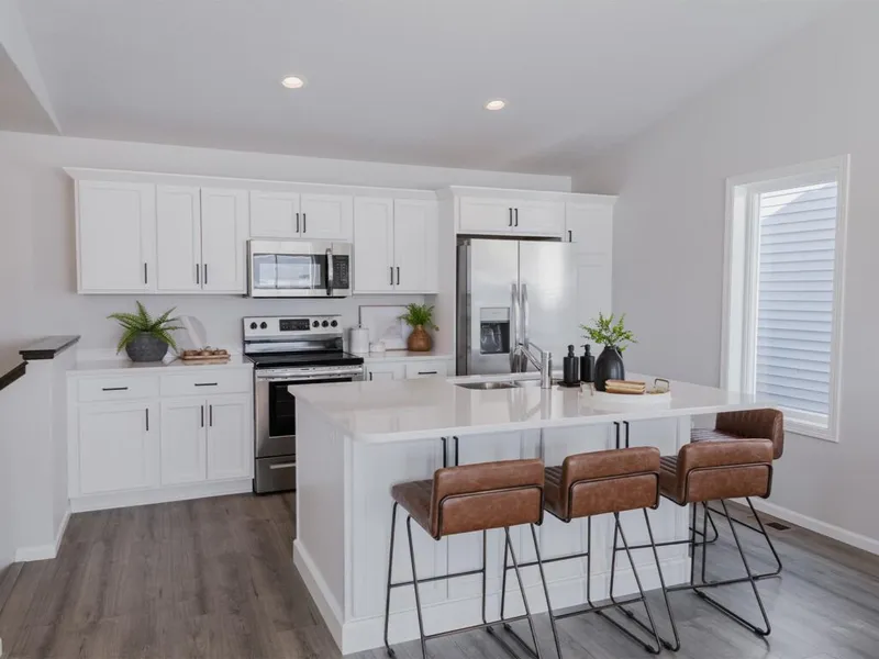 White shaker-cabinet kitchen with stainless appliances, island, and brown leather bar stools