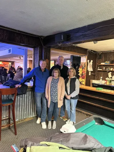 Four adults posing together inside a dimly lit bar with wood-paneled walls and a pool table