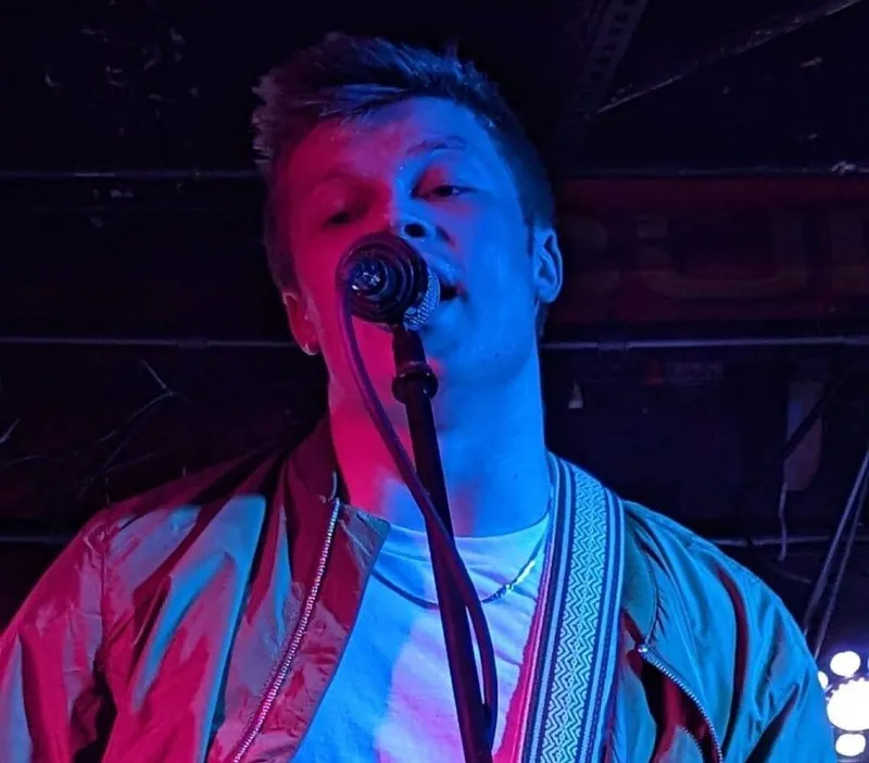 Young male vocalist singing into a mic under red and blue stage lights