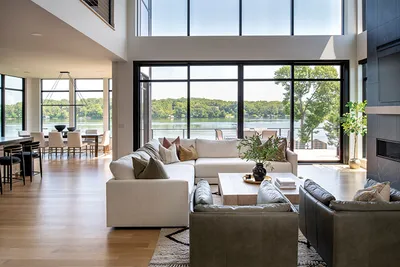 Bright open living room with white sectional sofa and floor-to-ceiling windows overlooking a lake