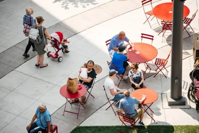 Aerial view of people gathered at red outdoor café tables on a sunny plaza