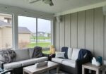 Screened porch with gray sectional sofa and coffee table overlooking a backyard