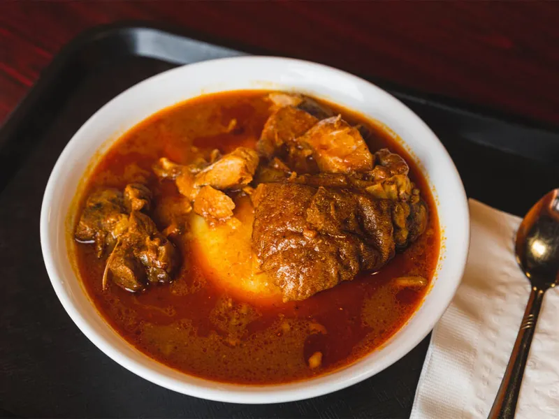 White bowl of rich red-broth meat stew on a black tray with a spoon