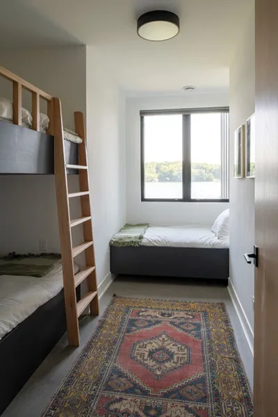 Narrow bedroom with wood-ladder bunk beds, a twin bed, and a patterned vintage rug