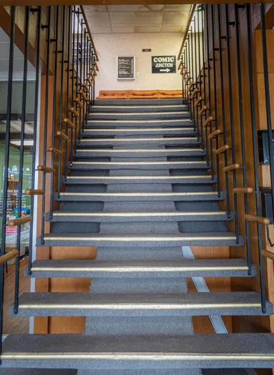 Carpeted staircase with wood and metal railings leading up to a Comic Junction sign