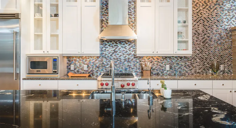 Modern kitchen with dark granite island, mosaic tile backsplash, and white cabinetry