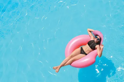 Woman in black bikini and sunglasses relaxing on a pink inflatable ring in a bright blue pool