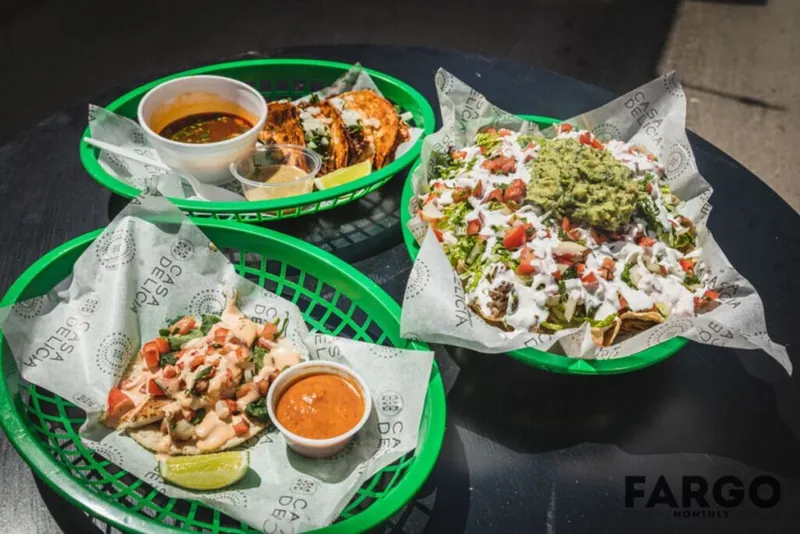 Three green plastic baskets of tacos and nachos topped with guacamole, pico de gallo, and sour cream