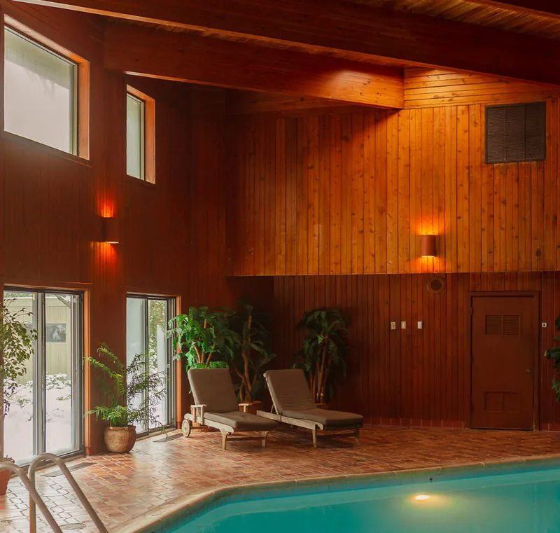 Indoor pool with two lounge chairs beside warm wood-paneled walls and tropical plants