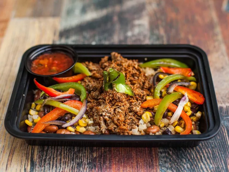 Black takeout tray with shredded meat, sautéed peppers, corn, beans, and a side of salsa