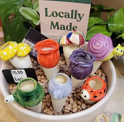 Colorful ceramic animal and mushroom plant stakes displayed in a bowl with a 'Locally Made' sign