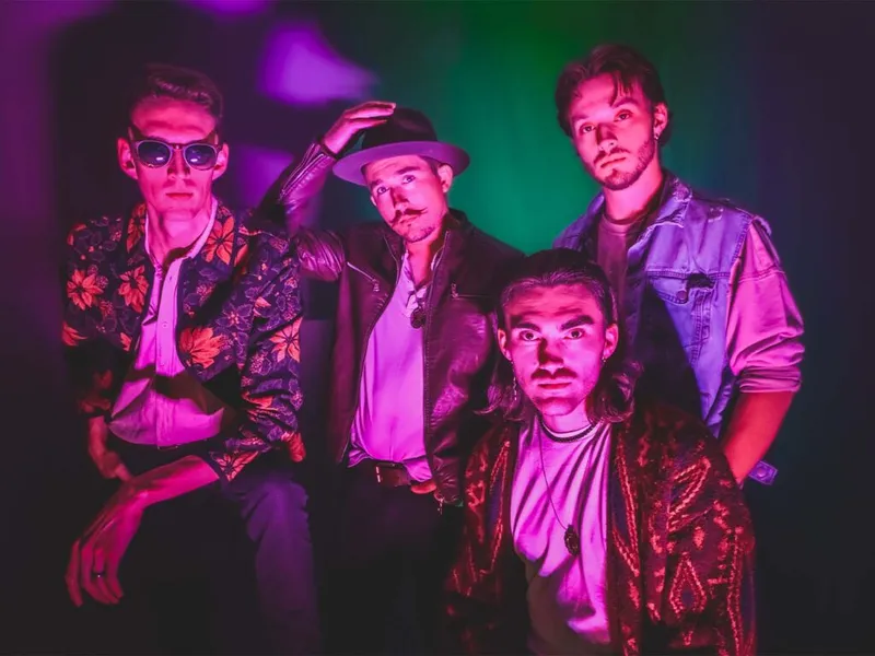 Four young men in eclectic jackets pose under moody purple and green lighting