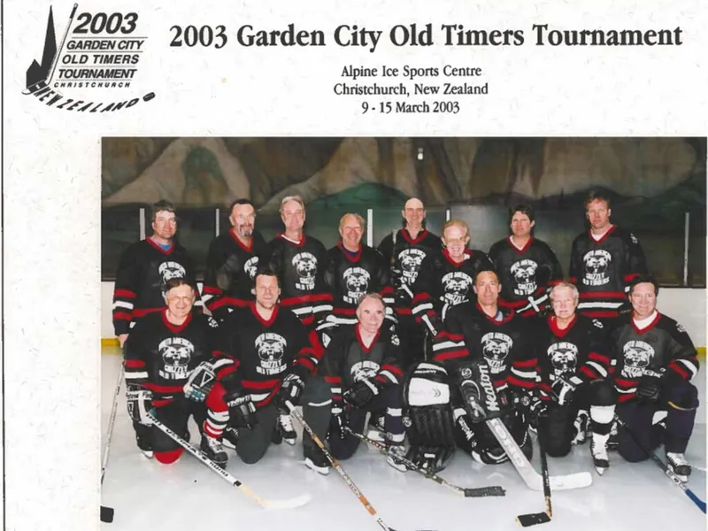 Men's ice hockey team posed on rink ice in matching black and red jerseys with sticks