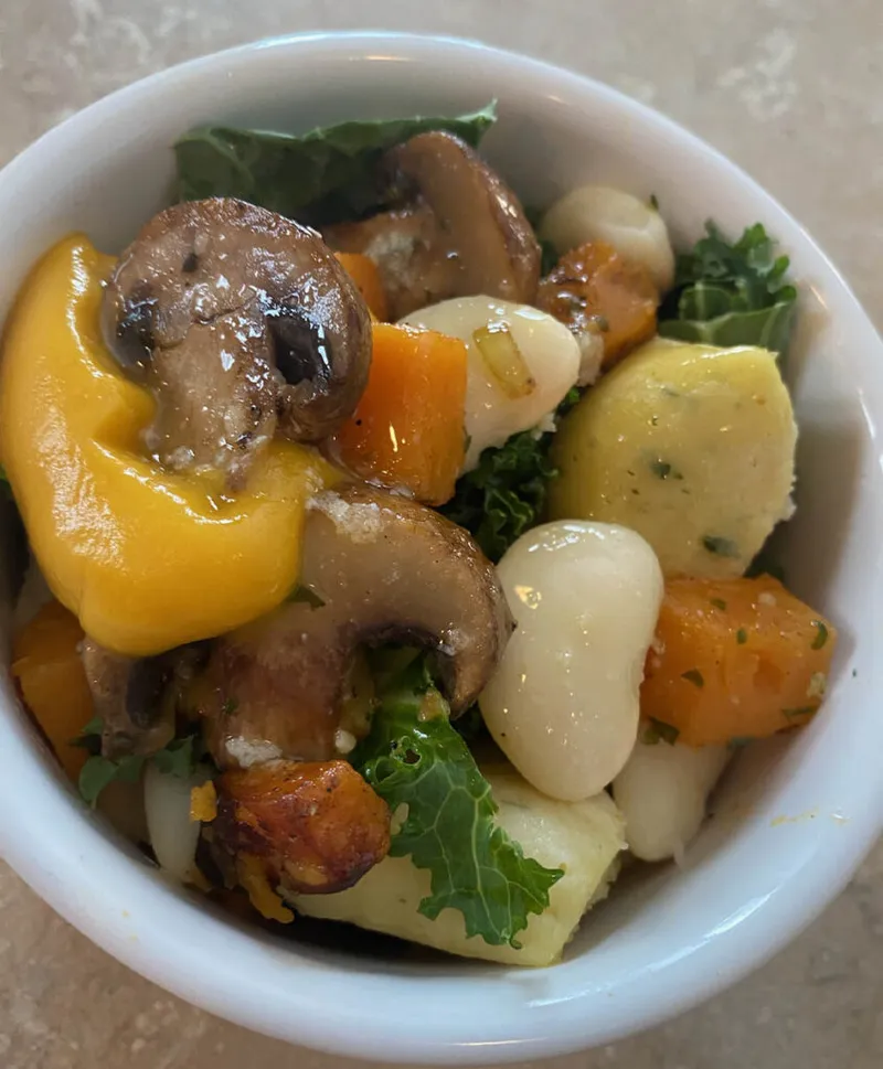 White bowl filled with sautéed mushrooms, yellow pepper, kale, carrots, and white beans