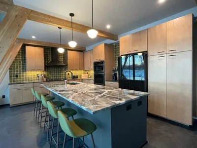 Modern kitchen with marble island, green bar stools, and light wood cabinetry