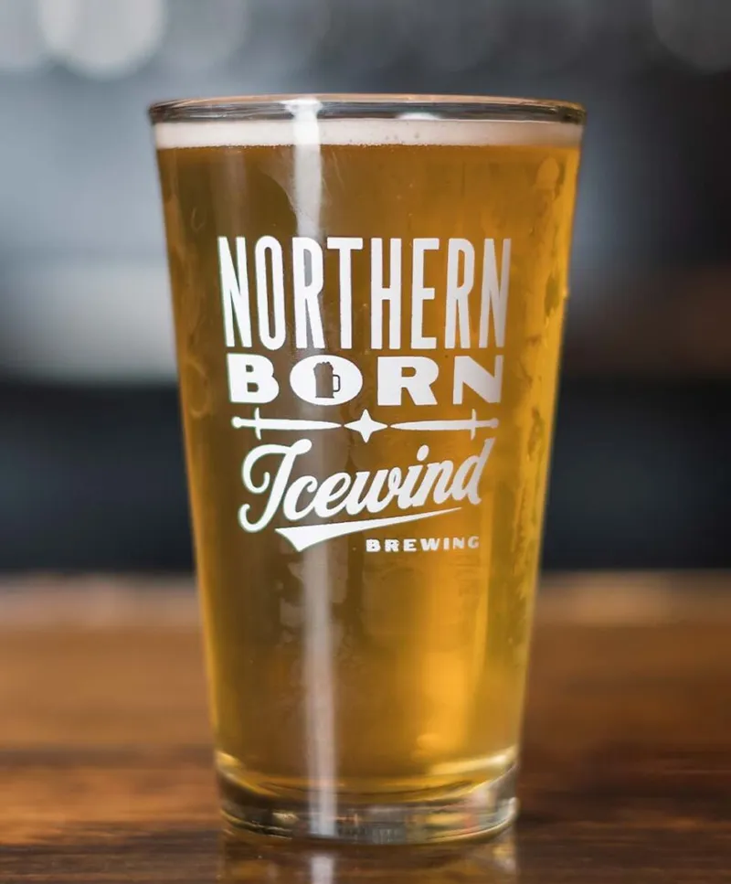 Pint glass of golden beer branded Northern Born Icewind Brewing on a wooden bar