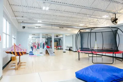 Bright therapy gym with a large trampoline, colorful hammocks, and a blue floor cushion