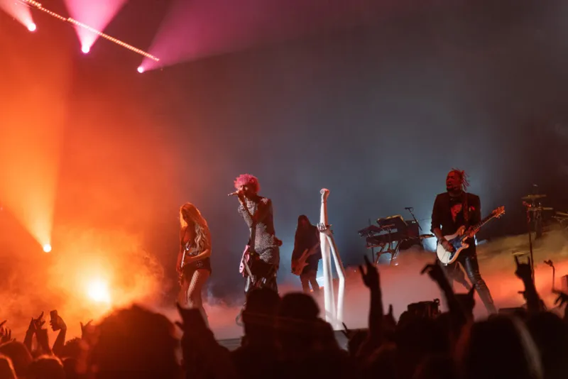 Rock band performs on a smoky stage bathed in orange and pink stage lights before a crowd
