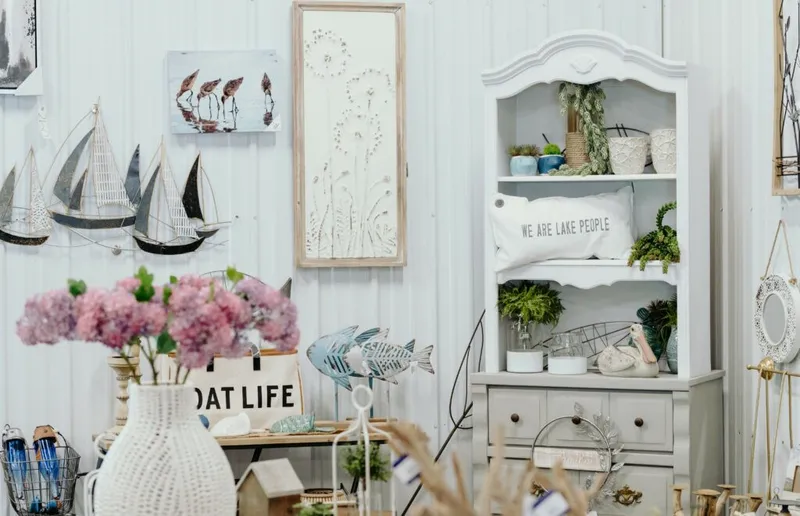 White hutch and coastal-themed décor including sailboat wall art, a 'We Are Lake People' pillow, metal fish, and pink