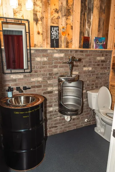 Rustic bathroom with a black barrel sink, keg urinal, and brick accent wall