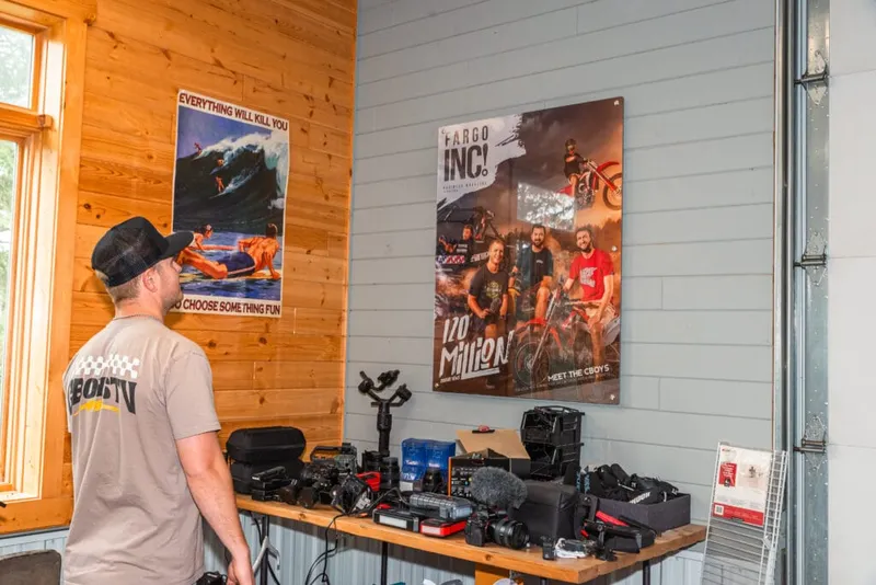 Man in baseball cap views a Fargo Inc. magazine poster above a table of camera gear