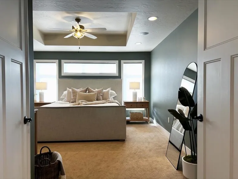 Styled bedroom with sage green walls, upholstered bed, tray ceiling, and leaning floor mirror