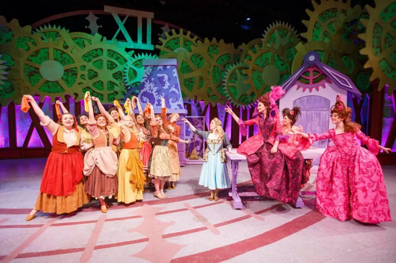 Stage performers in colorful period costumes amid giant gear backdrop during a theatrical production