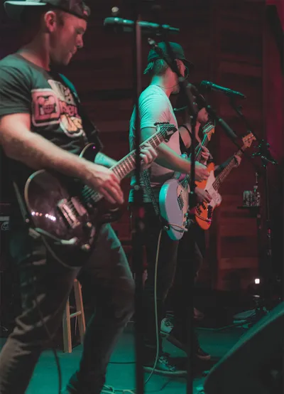 Three guitarists performing on a dimly lit stage under green and red lights