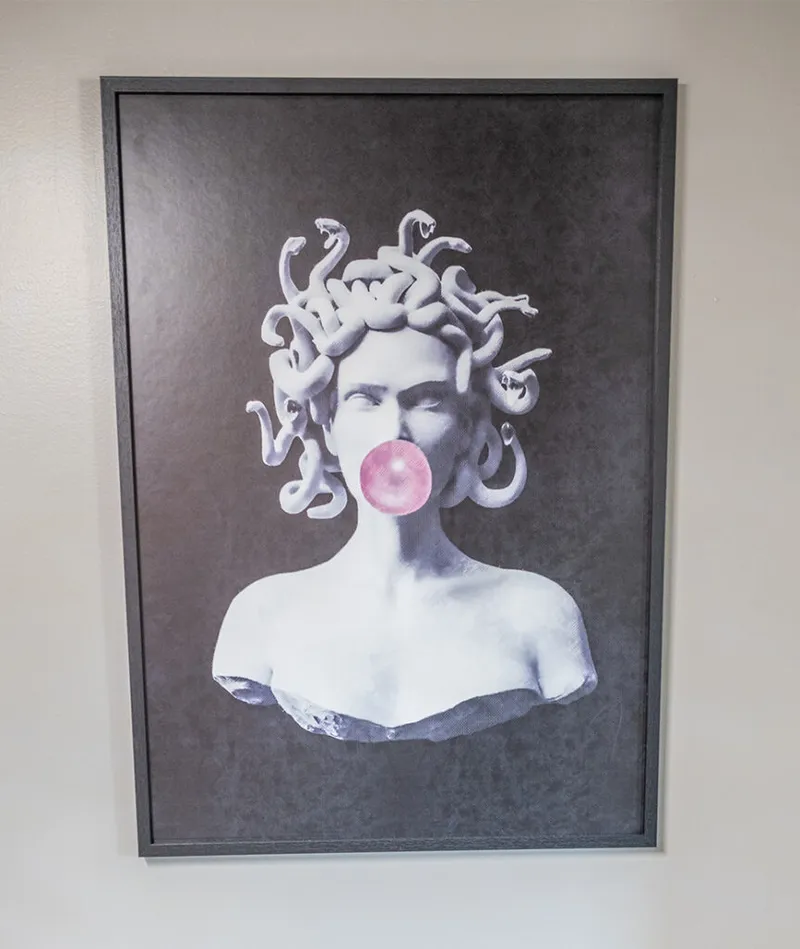 Framed pop-art print of a classical Medusa bust blowing a pink bubble, hung on a white wall