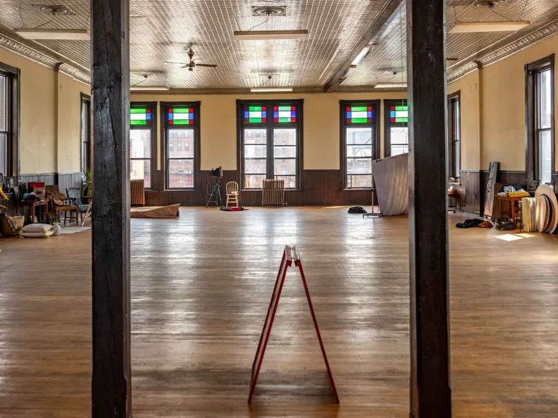 Spacious historic hall with wood floors, ornate tin ceiling, and colorful stained-glass transom windows