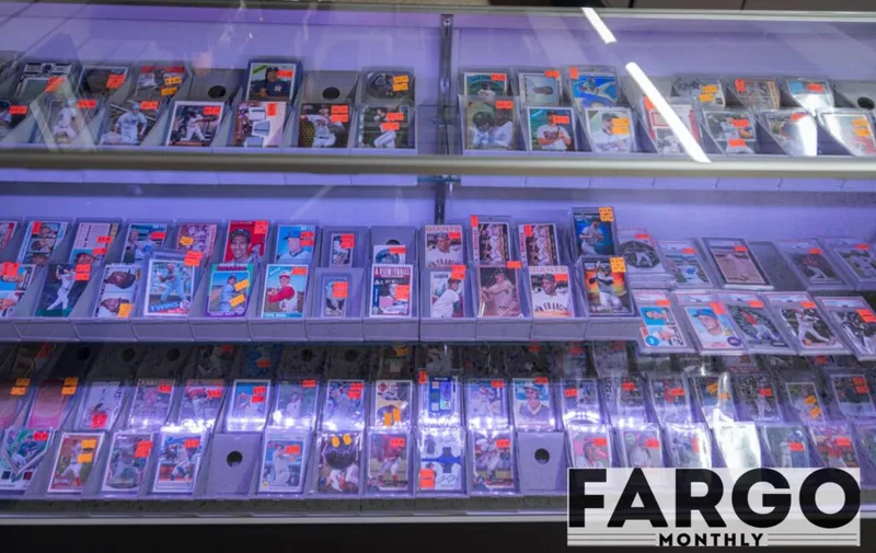 Baseball cards with orange price tags displayed across lit glass display case shelves